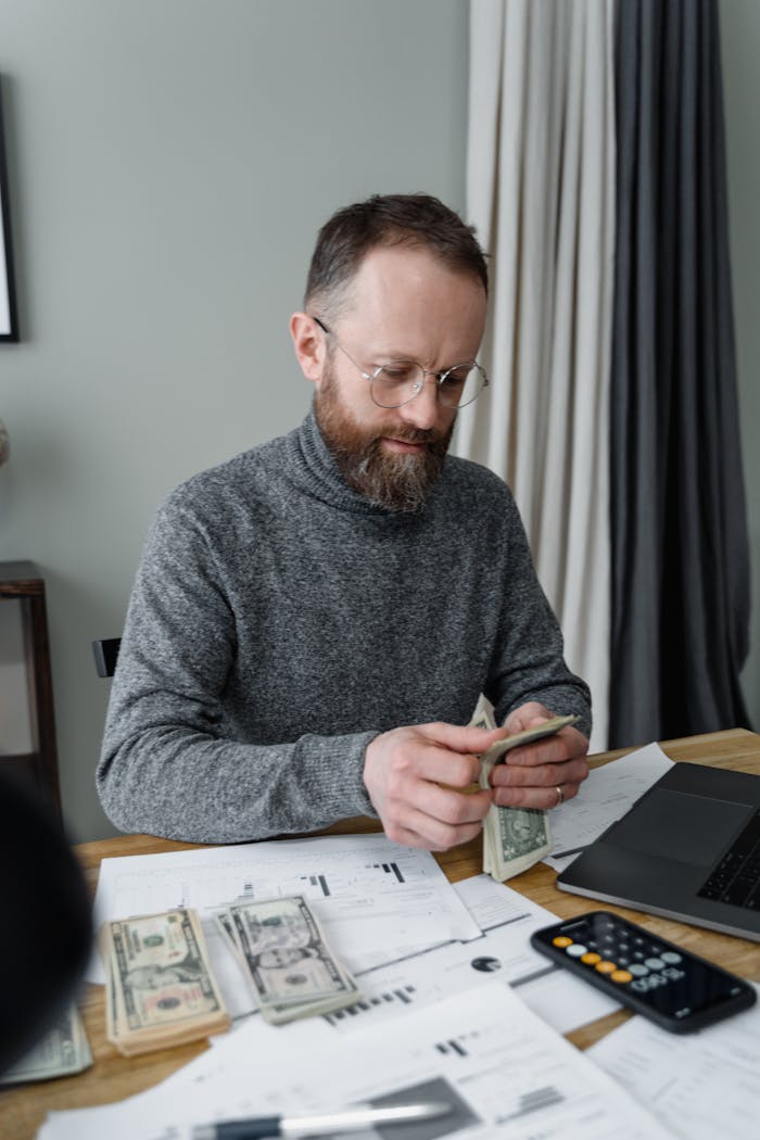 why-choose-us Bearded man in gray shirt counting dollar bills at office desk.